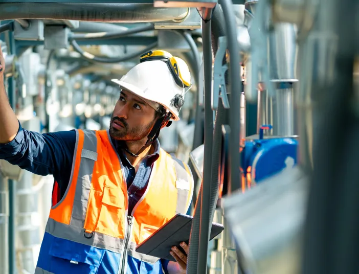 Gebäudetechniker in orangener Sicherheitsweste schraubt an den Geräten rum.